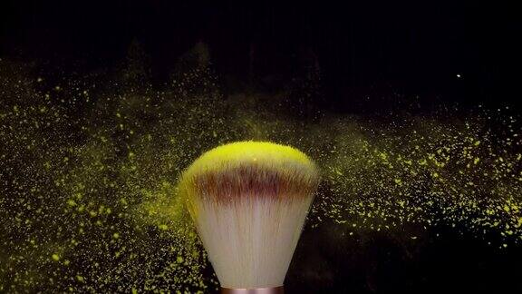 化妆刷与黄色粉末爆炸在黑色背景超级慢动作