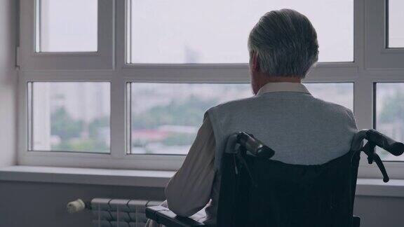 残疾老人独自坐在轮椅上从窗户望出去