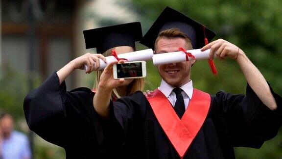微笑的男女毕业生用智能手机拍摄视频玩得开心