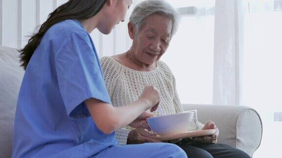 亚洲年轻女性护理护士给82岁高龄的亚洲老奶奶送早餐在家里照顾者