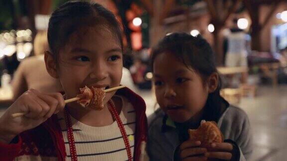 亚洲姐弟小女孩在泰国夜市街头小吃吃热狗美味的街头小吃