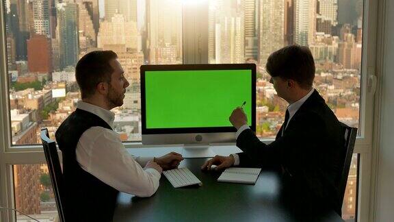 两个年轻的商人正在谈生意办公室用绿屏电脑显示器背景中的大城市创新增长财富资本主义