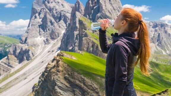 一名女游客在徒步旅行结束后休息喝着一瓶水