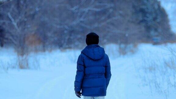 冬天一个穿着冬季夹克的年轻人正在森林附近散步冬天走了后视图