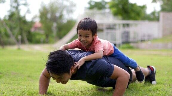 亚洲父亲在户外做俯卧撑让小男孩躺在他的背上