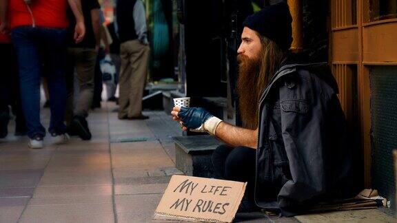一个无家可归的人拿着写着“我的生活我的规则”的纸板在拥挤的街道上乞讨