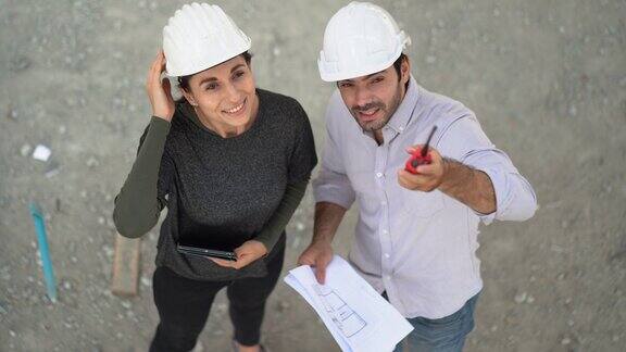 俯视图建筑师和工头妇女讨论平板和文件在施工现场承包商工人与建筑工人在室内检查一对夫妇正在检查在建的房子