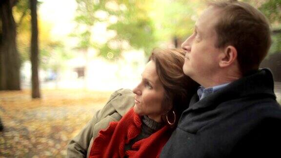 在一个晴朗的秋日一对情侣坐在公园的长椅上拥抱对方