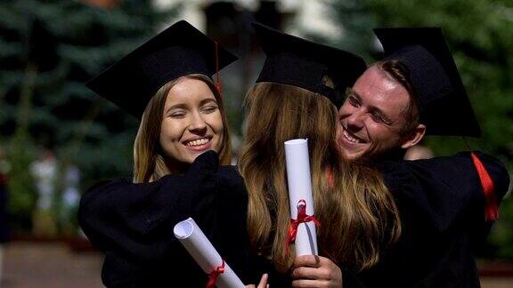 朋友们身着学术礼服的毕业生们互相祝贺、拥抱