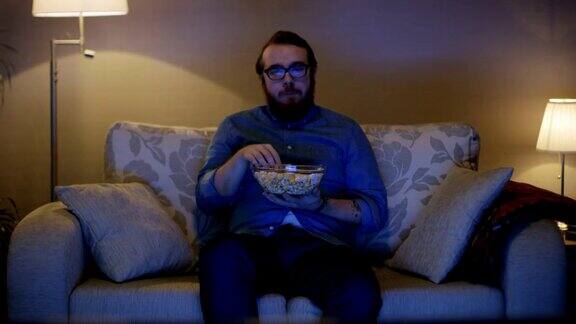 一个男人坐在客厅的沙发上一边吃着爆米花一边看电视落地灯打开