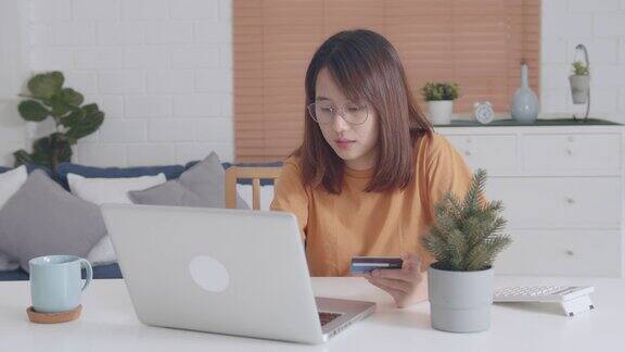 漂亮的年轻亚洲女人手打字信用卡号码的笔记本电脑