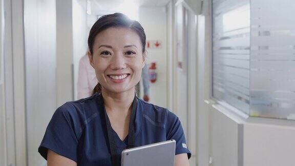 在繁忙的医院走廊里女护士穿着手术服手持平板电脑