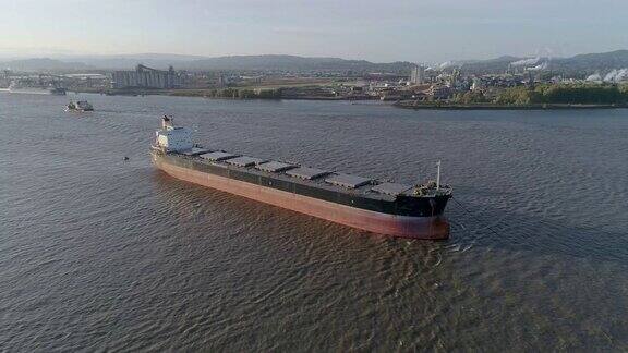 停靠在美国俄勒冈州和华盛顿州边界的哥伦比亚河上的货船背景中有一艘小船驶过无人机空中低空视频与平移摄像机运动