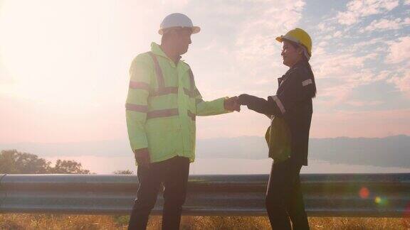 一名工程师戴着防护头盔在电力涡轮机的背景下在田野里握手