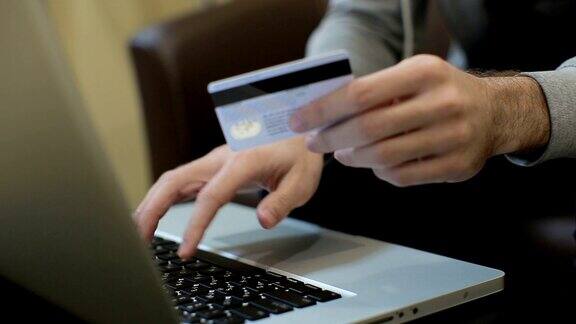 男人付账单网上购物插入信用卡号码一名男子使用笔记本电脑和信用卡在网上购物近距离
