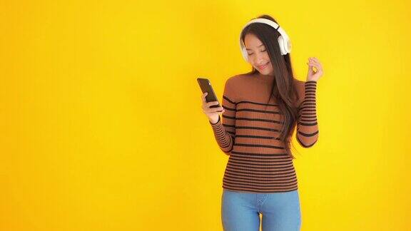 年轻的亚洲女性用耳机或耳机听黄色背景音乐