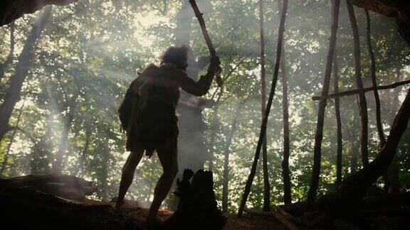穿着兽皮的原始穴居人手持石尖矛站在洞穴入口处俯瞰史前森林准备狩猎动物猎物尼安德特人在丛林中狩猎