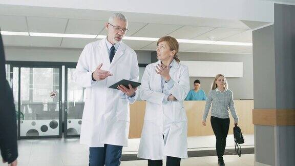 在医院里忙碌的医生一边聊天一边用平板电脑在大楼里走动在后台病人与接待员的谈话新型现代化、功能齐全的医疗设施