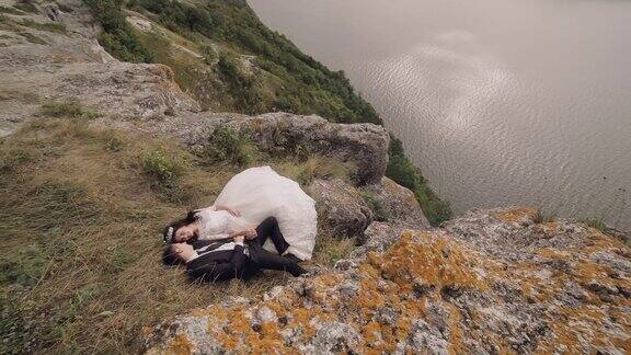 一对年轻美丽的新婚夫妇一起躺在海边山上的斜坡上可爱的新郎和新娘慢动作