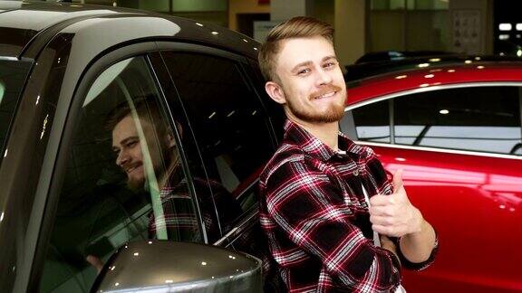 英俊的男子显示大拇指靠在一辆新车在经销商