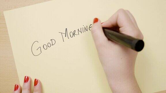 年轻女性的手写早上好并画一个笑脸在黄色纸上与黑色马克笔