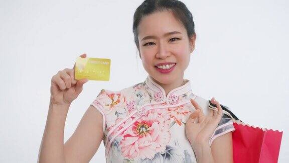中国亚洲妇女在春节期间用信用卡购物手拿购物袋白色背景穿着旗袍白色花卉服装