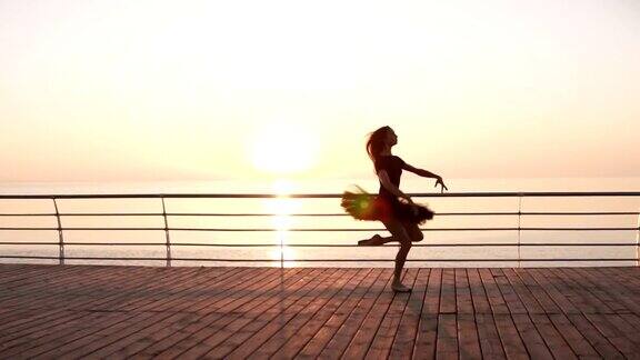 年轻女子穿着黑色芭蕾舞裙在海边跳芭蕾舞丛林阳光迷人的芭蕾舞演员在练习跳跃侧视图慢动作