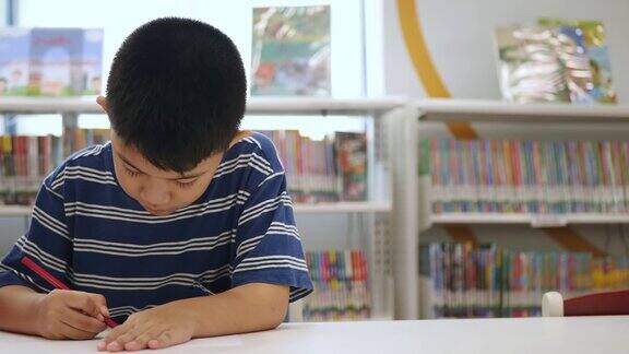 亚洲男孩坐在图书馆的桌子上用彩色铅笔和画卡通创意教育和自学