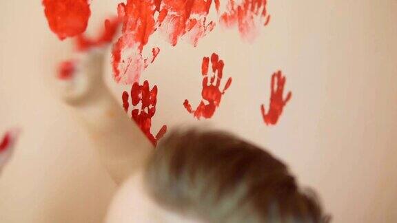 快乐可爱的小男孩在墙上留下他的红色手印玩得很开心年轻的幸福的家庭母亲和孩子Slowmotion