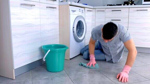 疲惫的男人戴着橡胶手套坐在厨房里擦洗地板
