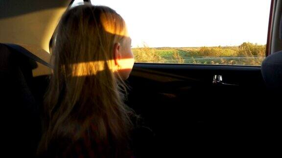 年轻的白人女孩开车缓慢的运动关注汽车窗外的田野和乡村景色秋天的日落