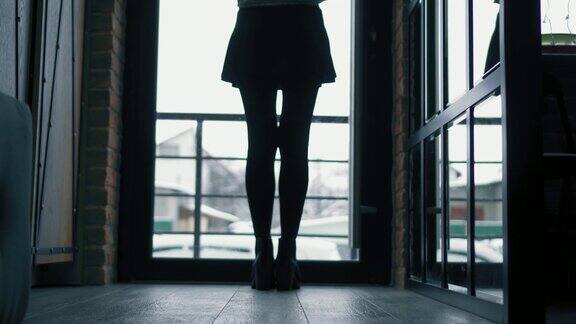 一个穿着黑色靴子的女人正沿着黑暗的走廊从摄像机走到门口向外面看了一眼然后又走了回去