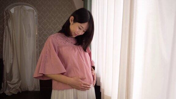 年轻孕妇在帘子附近触摸她的腹部