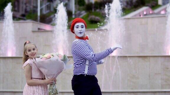 滑稽的哑剧演员和小女孩拿着一束鲜花在喷泉的背景下