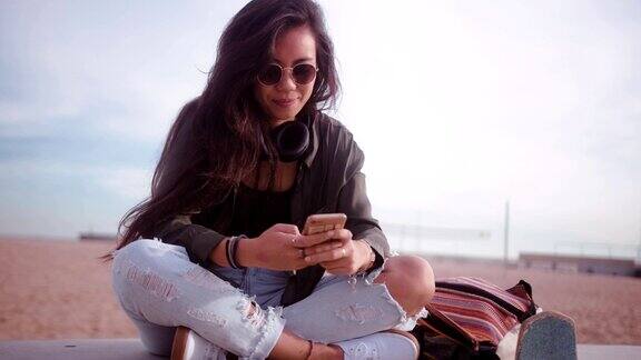 美丽的时髦的亚洲女孩与智能手机聊天在海滩上