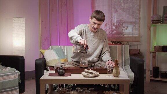 一位中年男子拿着一把已经泡好的茶茶壶将茶倒入玻璃杯中喝起茶来