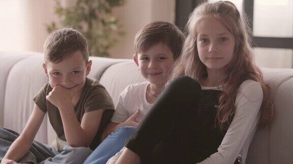 一个积极的女孩和两个男孩坐在沙发上看着摄像机