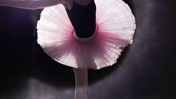 优雅灵活的女孩在她的尖头芭蕾舞鞋在聚光灯下的黑色背景在工作室专业芭蕾舞演员穿着芭蕾舞短裙和尖头鞋展示经典芭蕾舞剧