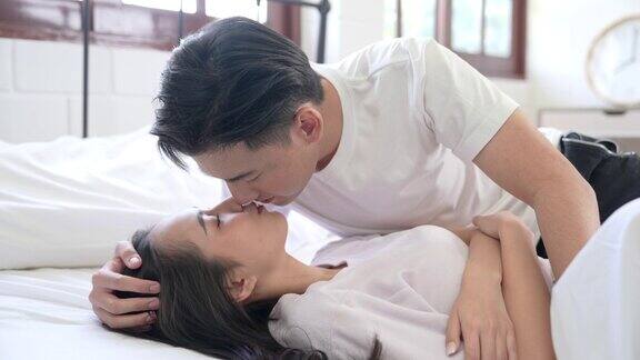 亚洲情侣早上躺在床上拥抱亲吻对方的脸颊