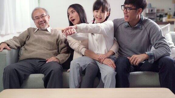 4K超高清倾斜:幸福的几代亚洲家庭一起在客厅的沙发上看电视