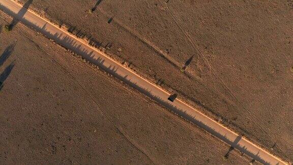 空中镜头:一辆黑色SUV正行驶在阳光明媚的沙漠里的土路上