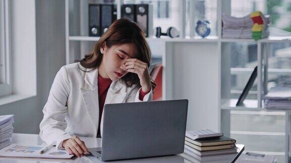 亚洲女性在笔记本电脑上工作时压力很大亚洲女商人在办公室头痛