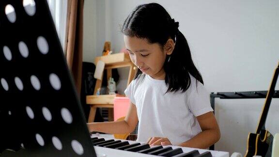 亚洲小女孩学习弹奏基本钢琴使用电子合成器键盘初学者音乐器乐自学在家