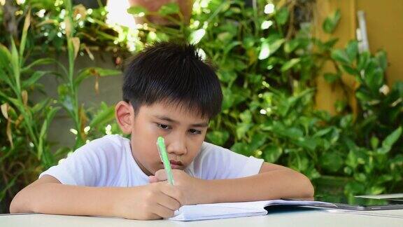 一个亚洲男孩用钢笔在笔记本上写作业