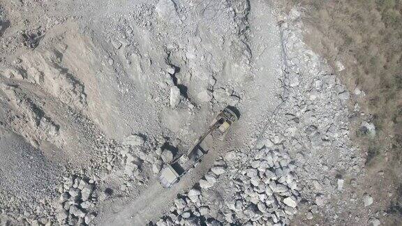 挖掘机将石块装进自卸卡车的高空垂直鸟瞰图