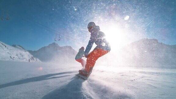 SLOMOTS两名滑雪板运动员在阳光下沿着雪道滑行使雪颗粒在空中飞舞