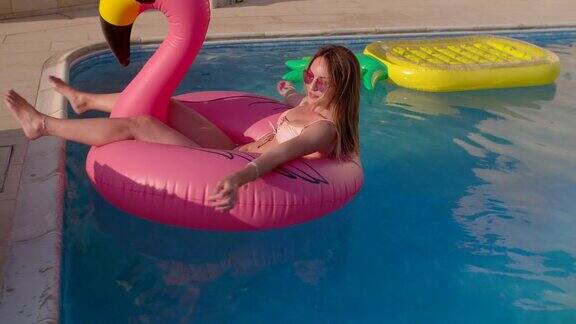 年轻女子漂浮在粉红色的火烈鸟充气游泳池