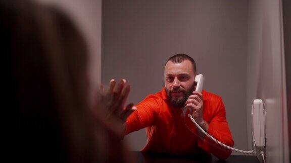 在监狱访问期间一名穿着连体服的囚犯和他的妻子将双手放在他们之间的玻璃上