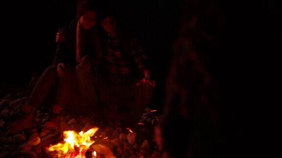 年轻夫妇晚上围坐在沙滩上的篝火旁