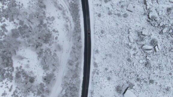 直接头顶无人机拍摄的一辆汽车在一条道路上行驶在一个下雪岩石沙漠景观在冬天